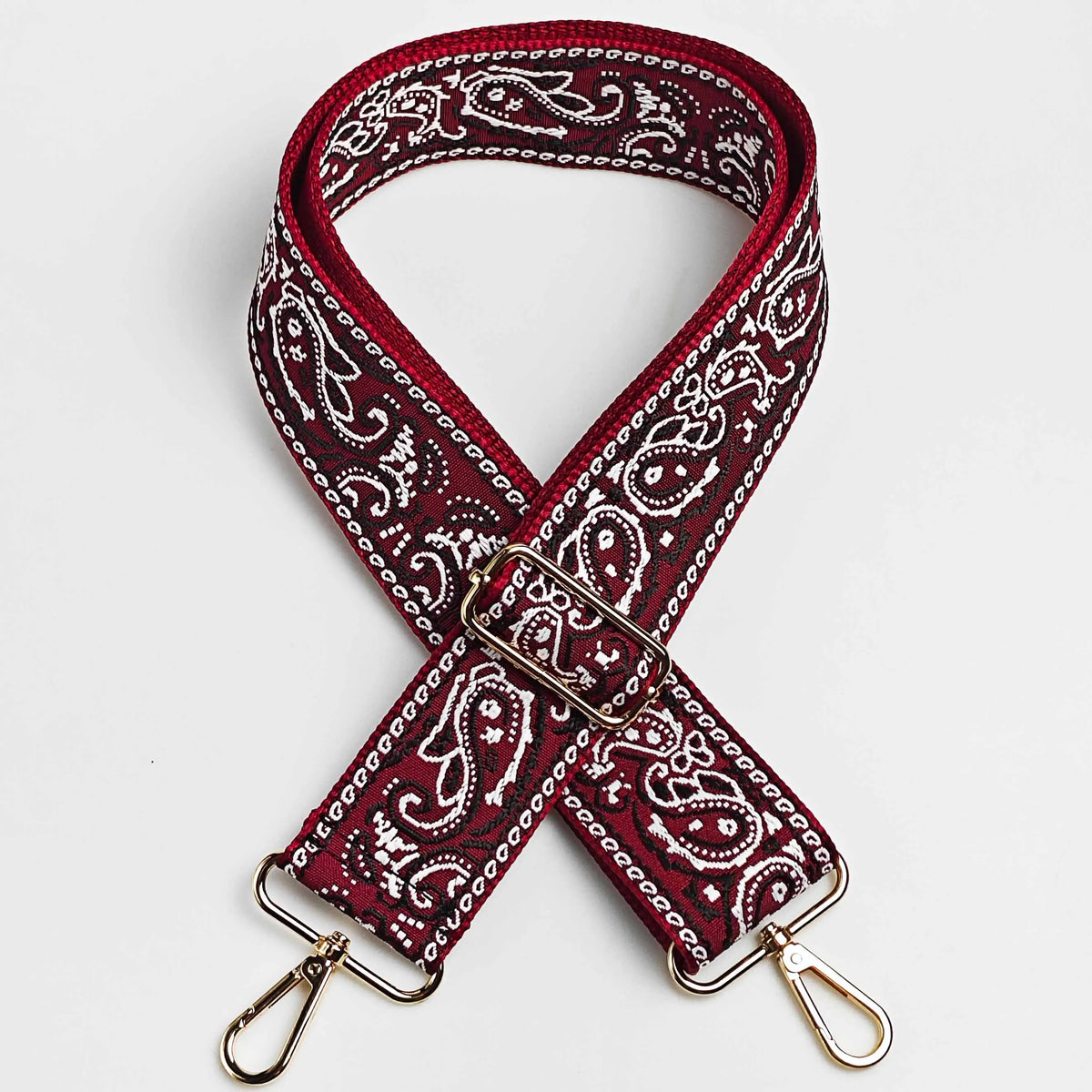 A maroon and white paisley jacquard bag strap with a gold-toned buckle and metal hardware.