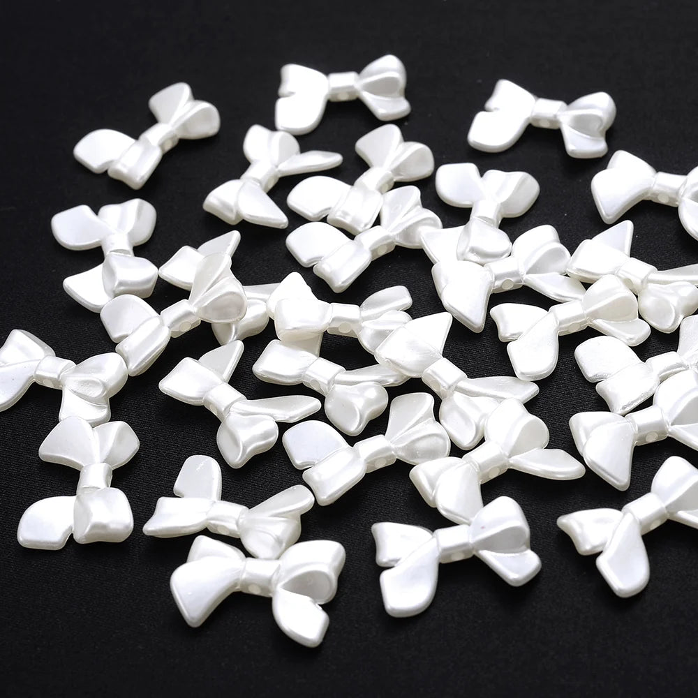 A pile of 100 white acrylic pearl spacer beads shaped like bows for jewelry making