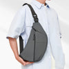 A person wearing a light blue shirt carries a black practical chest bag on their shoulder.