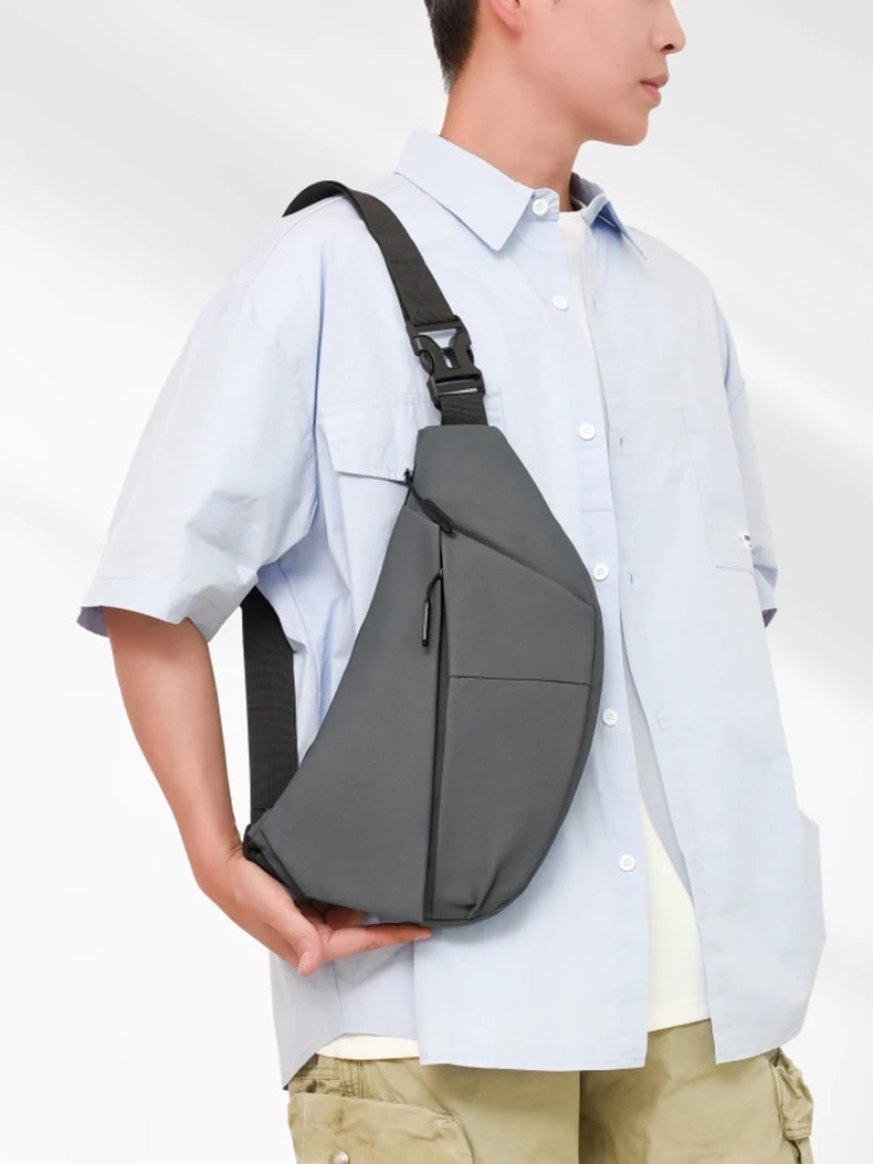 A person wearing a light blue shirt carries a black practical chest bag on their shoulder.