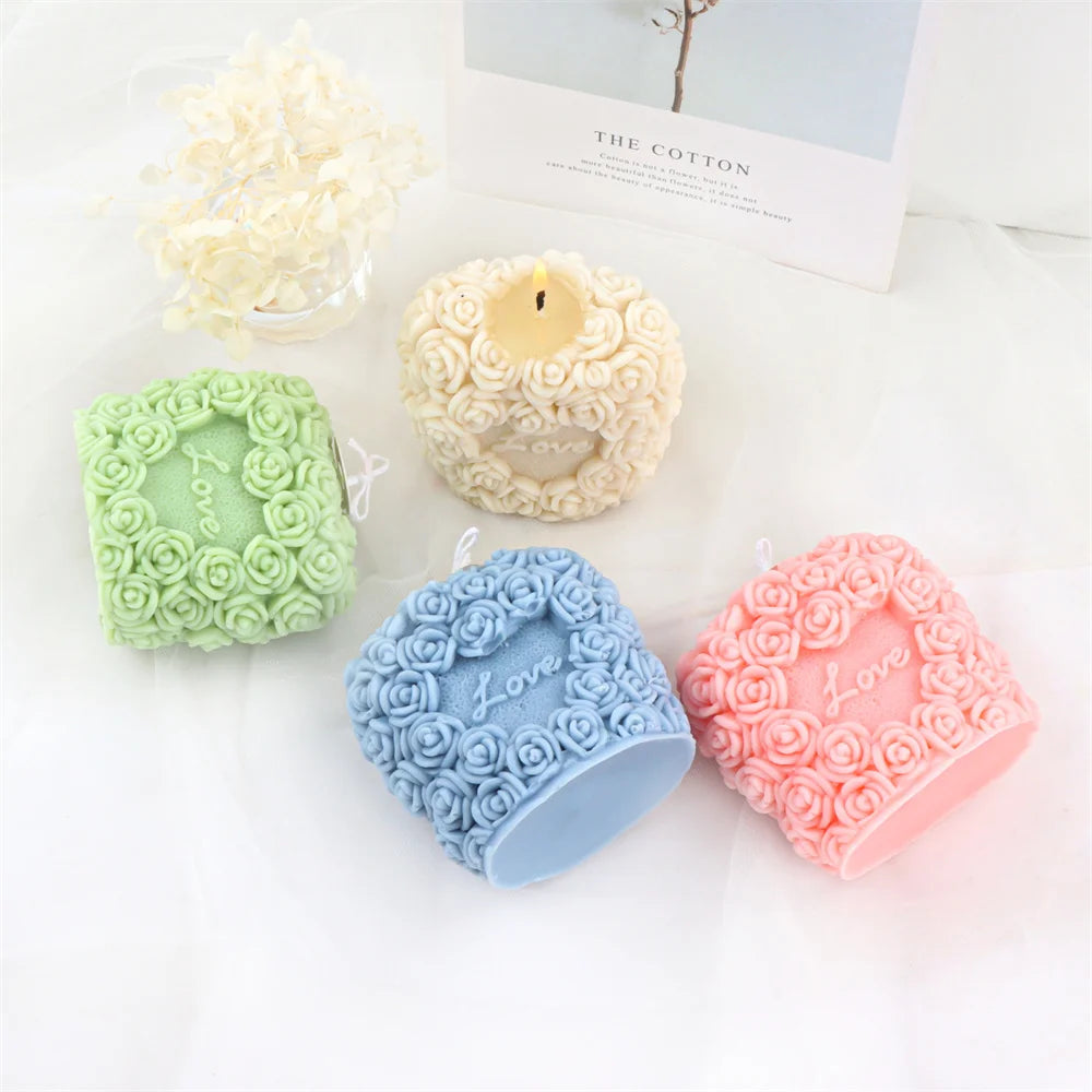 A collection of three silicone molds shaped like roses in green, blue, and pink, alongside a yellow pillar candle.