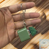 A hand holds an interactive fidget keychain with a green plastic component and a silver chain.