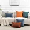 A set of two retro corduroy patchwork throw pillow covers in shades of orange, teal, and gray displayed on a white sofa.