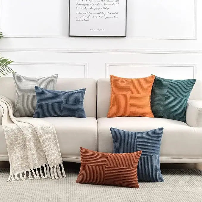 A set of two retro corduroy patchwork throw pillow covers in shades of orange, teal, and gray displayed on a white sofa.