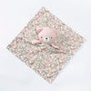 A pink teddy bear stuffed animal resting on a floral patterned fabric square.
