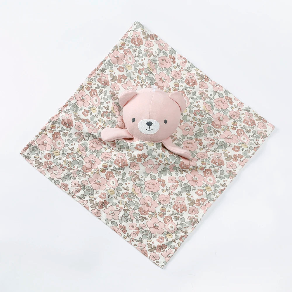 A pink teddy bear stuffed animal resting on a floral patterned fabric square.