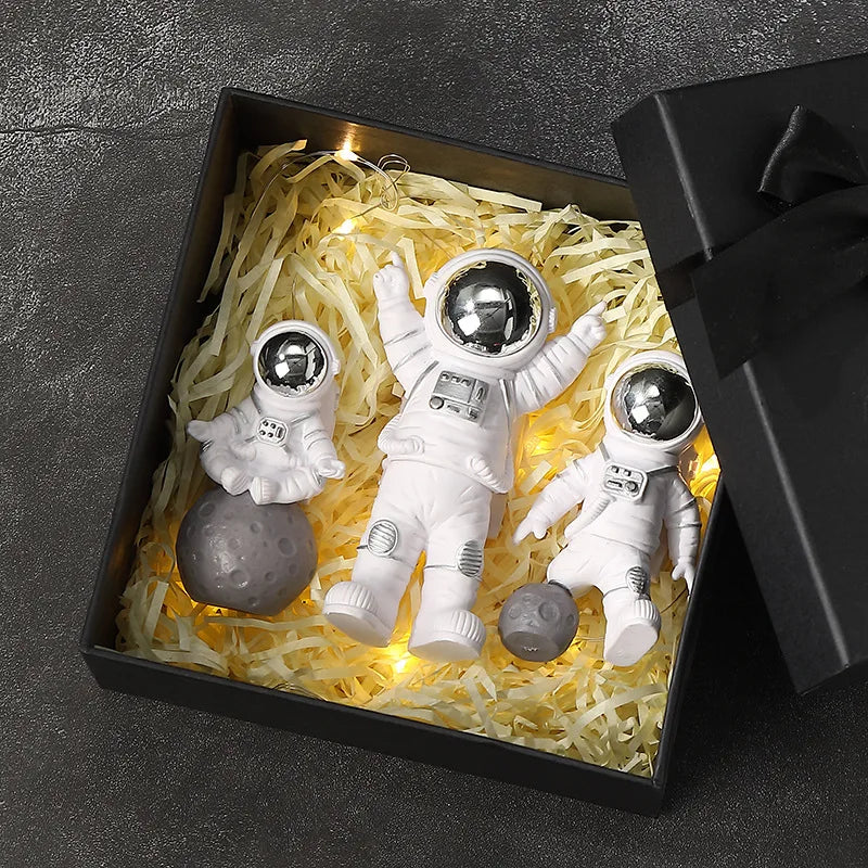 A set of handcrafted astronaut figurine resin spacemen desk decor displayed in a black box with glowing yellow filler.