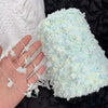A hand is holding a fluffy light blue and white variegated cotton blend yarn for knitting or crochet.