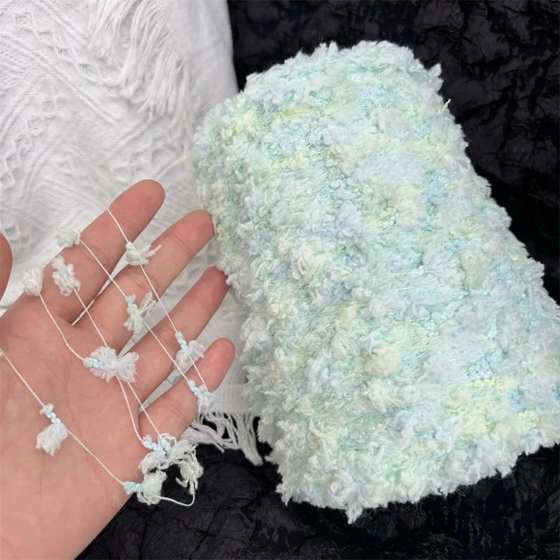 A hand is holding a fluffy light blue and white variegated cotton blend yarn for knitting or crochet.
