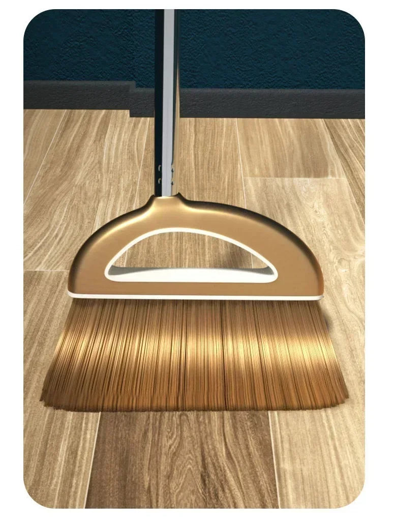 A golden broom and dustpan set with a floor wiper resting on a wooden floor.