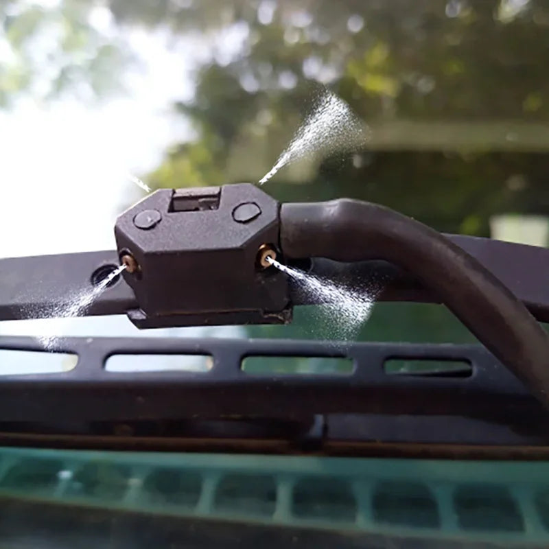 A close-up of two car windshield washer nozzles being sprayed onto a surface.