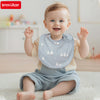 A smiling baby wearing a light blue cotton bib with white animal designs, sitting on a white rug.