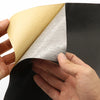 A hand is peeling a self-adhesive PU leather repair patch from a black material, showing the beige and gray adhesive side.