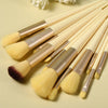 A set of thirteen makeup brushes with gold and natural hair bristles laid out on a light background.
