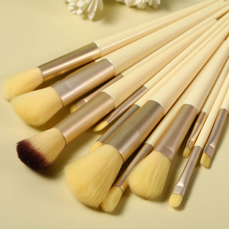 A set of thirteen makeup brushes with gold and natural hair bristles laid out on a light background.