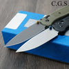 A folding knife with a drop point blade and a green handle is resting on a blue box.