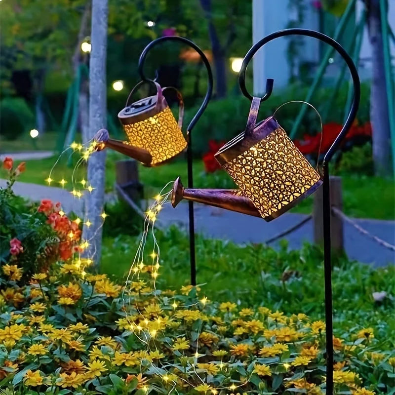 A vintage solar watering can garden light with a shepherd's hook is shown illuminating yellow flowers.