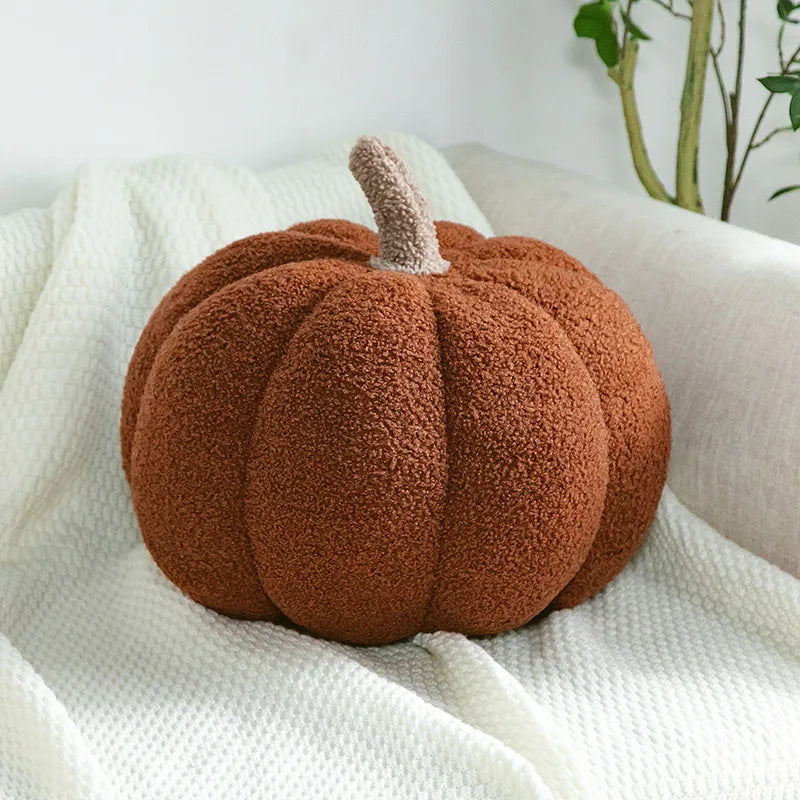 A round, textured brown pumpkin plush pillow with a fuzzy stem resting on a white knitted fabric.