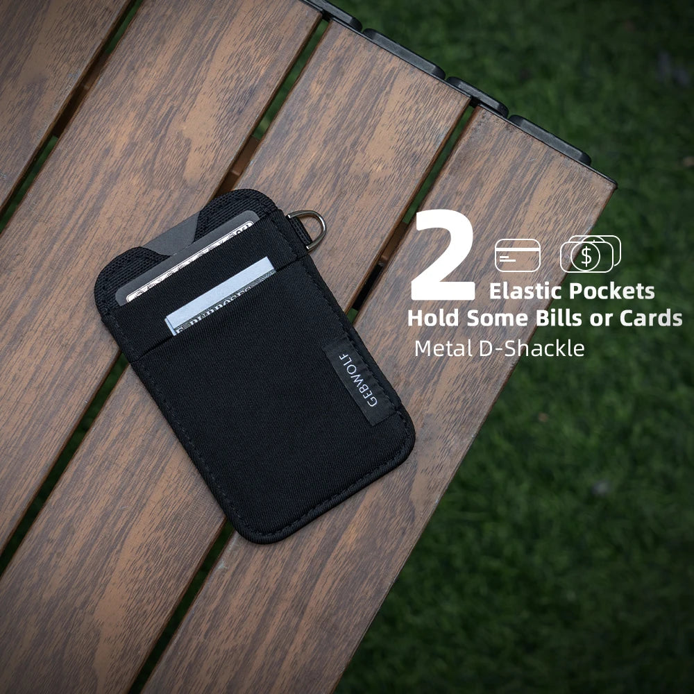 Porte-cartes minimaliste noire en nylon avec poches élastiques et griffe métallique sur une terrasse en bois.