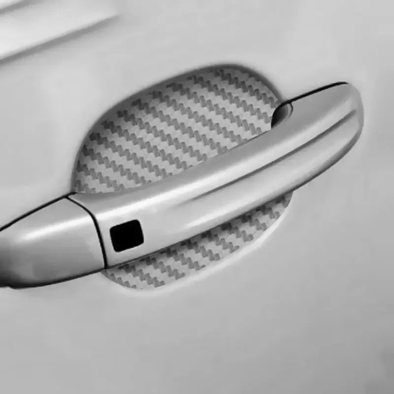 A close-up of a silver car door handle with a carbon fiber protective cover placed on it.