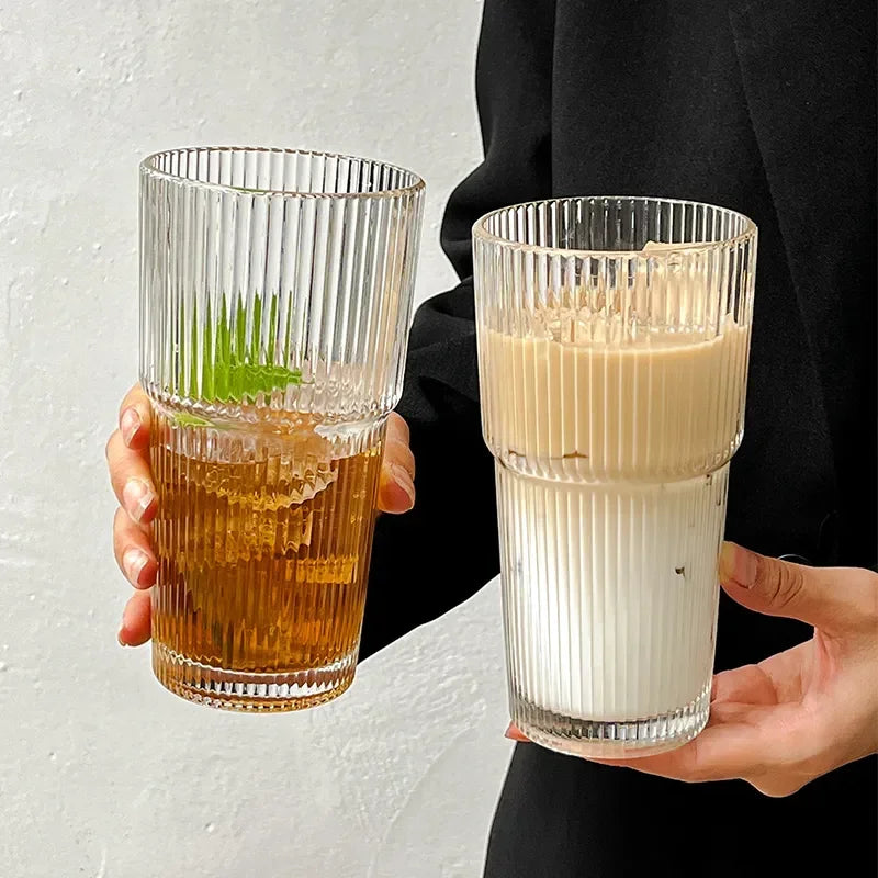 Une main tient un verre tumbler rayé haut rempli d'une boisson ambrée et d'une garniture verte.