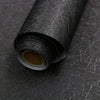 Roll of black self-adhesive wallpaper with a beige backing visible at the end