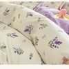 Nahaufnahme einer cremefarbenen Baumwoll-Decke mit einem lila lavendelfarbenen Blumenmuster auf einem Bett.