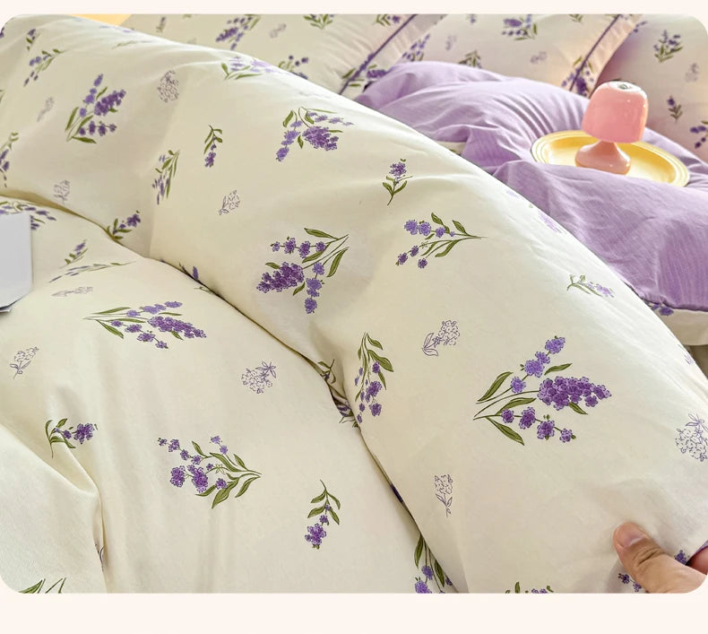 Nahaufnahme einer cremefarbenen Baumwoll-Decke mit einem lila lavendelfarbenen Blumenmuster auf einem Bett.