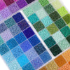 A variety of glass rice beads in various shades of green, blue, purple, and yellow are displayed in a partitioned kit.