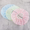 Three disposable waterproof shower caps in blue, green, and pink polka dots with a white elastic band.