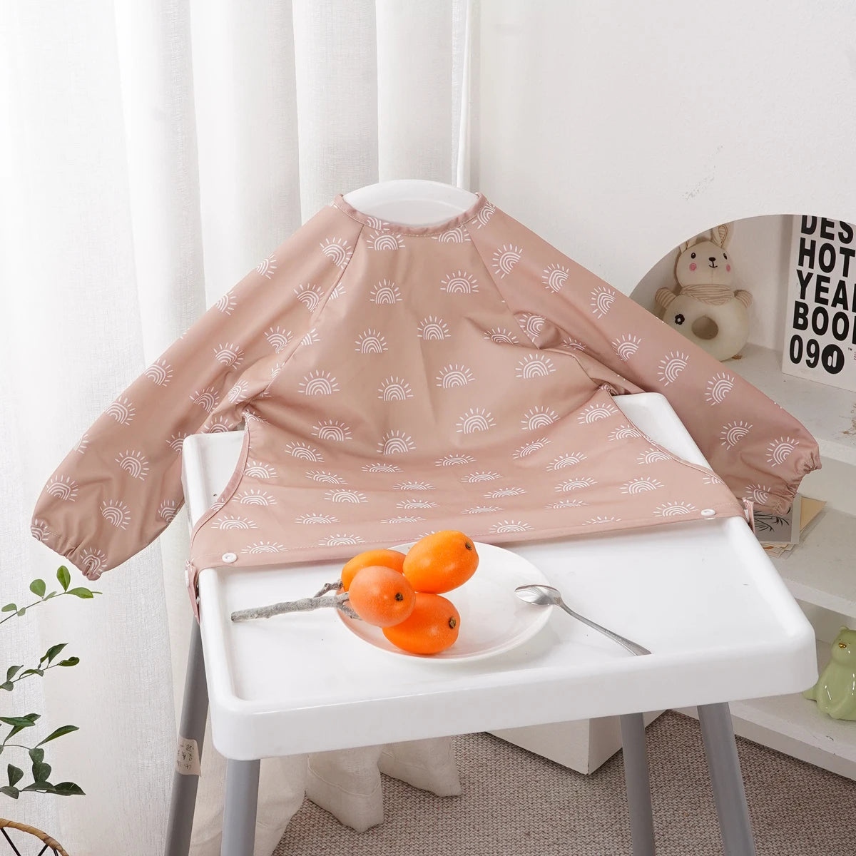 A light pink long-sleeve waterproof baby bib with a cute animal pattern displayed on a white table.