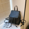 Mini sac à dos noir à cordon, exposé sur une surface blanche près d'un store.
