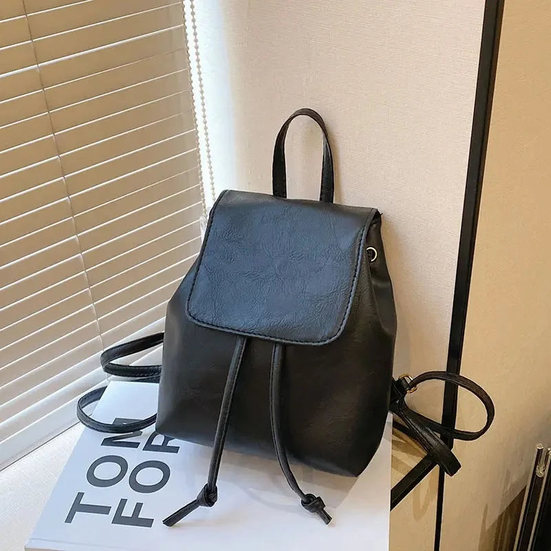 Mini sac à dos noir à cordon, exposé sur une surface blanche près d'un store.