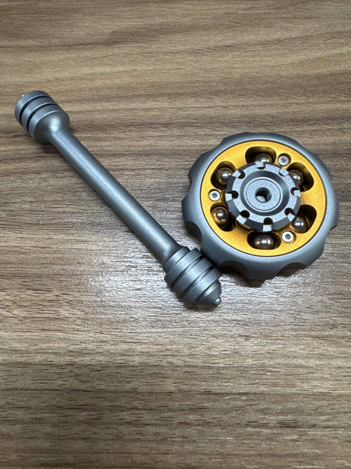 A metal fidget spinner with a long shaft and a circular weighted top, used for stress relief.