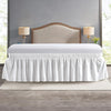 White elastic wrap-around bed skirt with ruffles displayed on a bed.