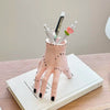 A pink resin Halloween hand planter and pen holder with black dots, holding several pens and a small flower.