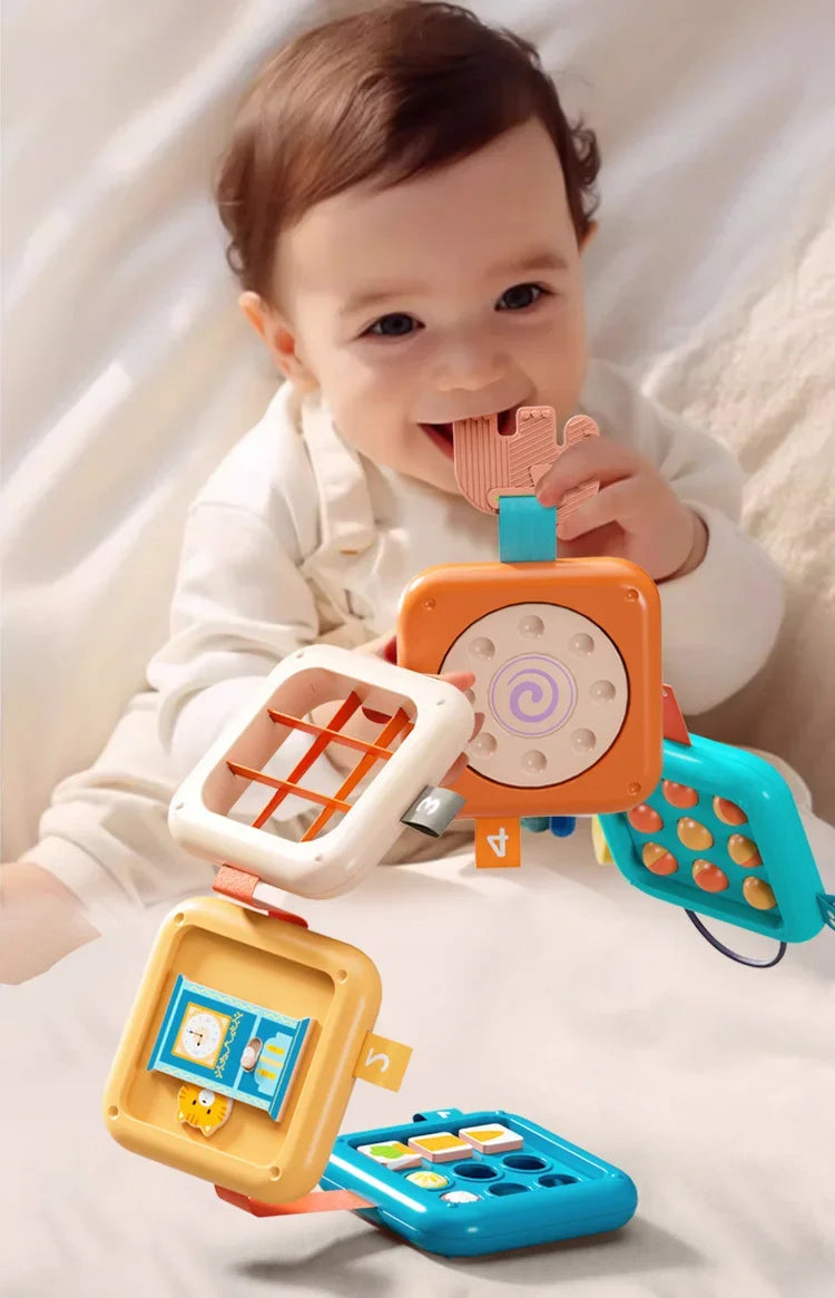 A baby is interacting with a colorful sensory folding activity cube and busy board designed for fine motor skills.