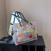 A clear transparent tote bag set with a decorative inner pouch and a mirrored surface displayed on a dark surface.