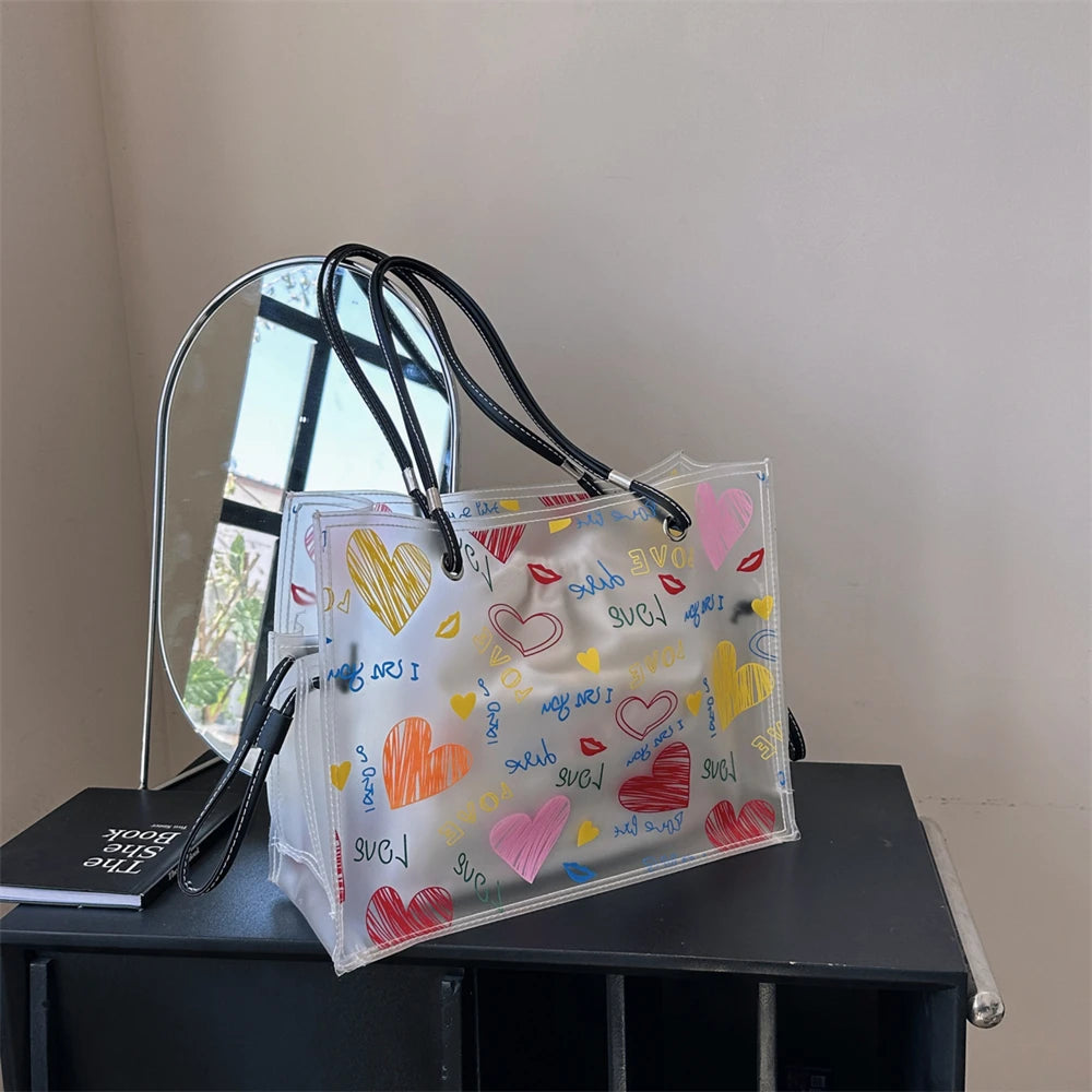 A clear transparent tote bag set with a decorative inner pouch and a mirrored surface displayed on a dark surface.