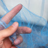 A hand holds a piece of light blue elegant lace canopy mosquito net fabric.