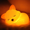 A glowing orange fox-shaped night light resting on a soft surface.