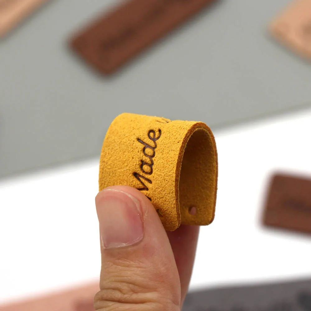 A hand holds a yellow felt label shaped like a heart with the word Made stitched onto it.