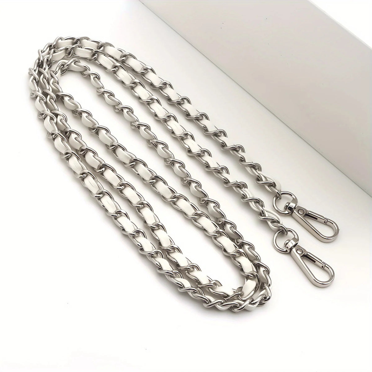 Silver metal chain purse strap with a secure buckle lying on a white surface.