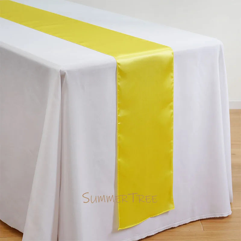 Elegant satin yellow table runner draped across a white tablecloth.