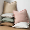 A stack of five boho fringe throw pillows in natural linen textures, including beige, pink, and sage green.