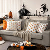A gray sofa decorated with orange and white Halloween themed throw pillows and a pumpkin on the floor.
