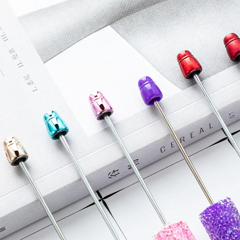 A collection of ten kawaii beaded ballpoint pens in various colors, including red, purple, and silver, resting on a white bac