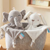 A gray elephant plush toy with a white rabbit plush toy and blankets sitting in a gray storage basket.