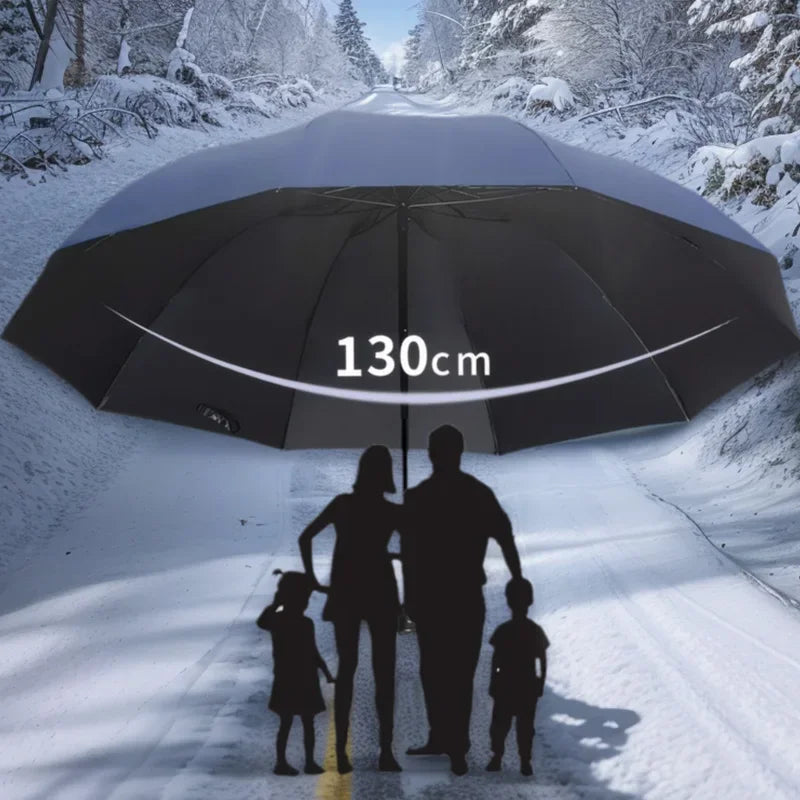 A large black folding umbrella is held over a snowy path with a family walking beneath it.