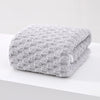 A thick, gray, textured plush bath towel folded neatly on a white surface.